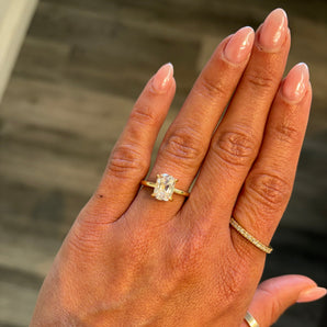 A close-up of a hand wearing a custom-made 14k gold elongated cushion old mine cut lab grown diamond solitaire engagement ring
