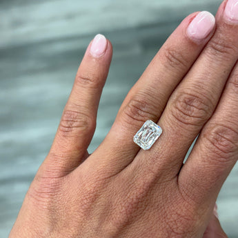 A loose 4.00ct cushion crisscut lab grown diamond resting on the ring finger of a hand