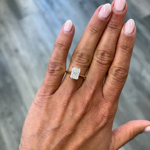 A close-up of a hand wearing a custom-made 14k gold radiant lab grown diamond solitaire engagement ring